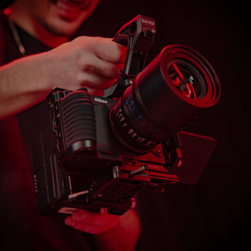 SHAPE Nikon ZR camera cage close-up showing 1/4-20 and 3/8-16 threaded mounting points in red cinematic lighting in lifestyle